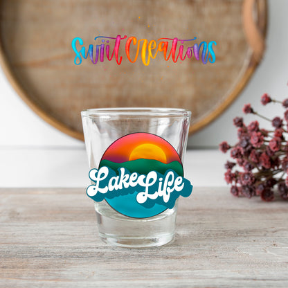Lake Life shot glass transfer on a clear glass beside a wooden barrel and dried flowers