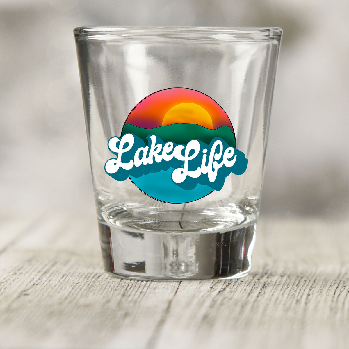 Lake Life shot glass UV DTF transfer with sunset over hills and water on a clear shot glass