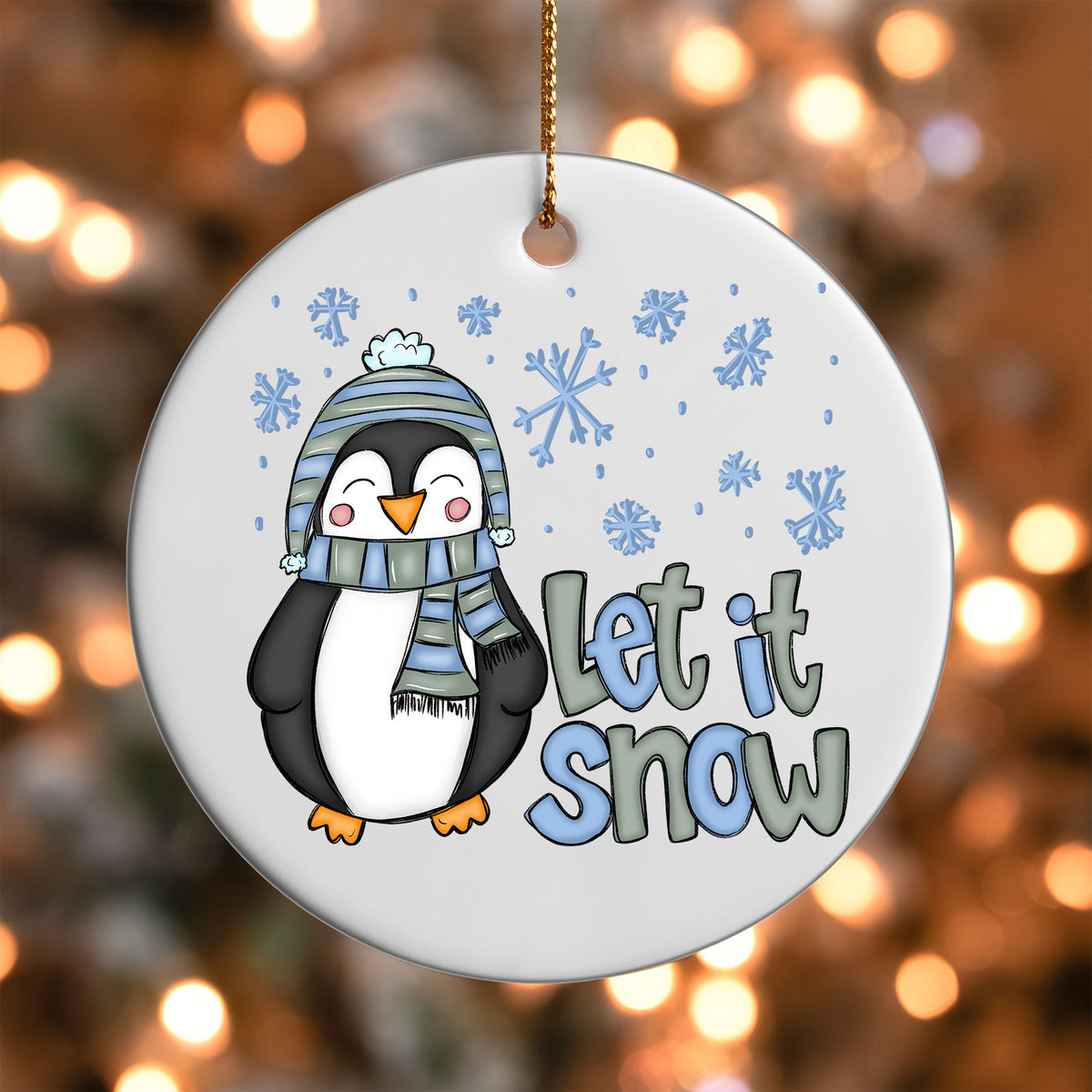 Let It Snow Penguin ornament UV DTF transfer on a round white ornament with a bokeh light background