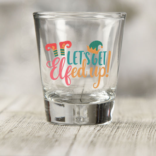 Let's Get Elfed Up shot glass UV DTF transfer with striped elf legs, curled shoes, and an elf hat on a clear shot glass