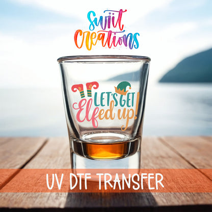 Let's Get Elfed Up shot glass UV DTF transfer on a filled shot glass on a dock by the water