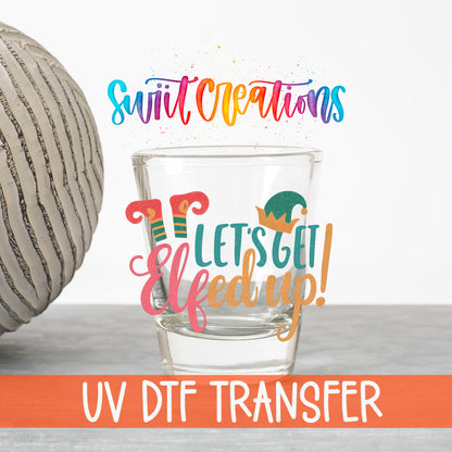 Let's Get Elfed Up UV DTF transfer on a clear shot glass with the Swiit Creations logo and UV DTF Transfer banner