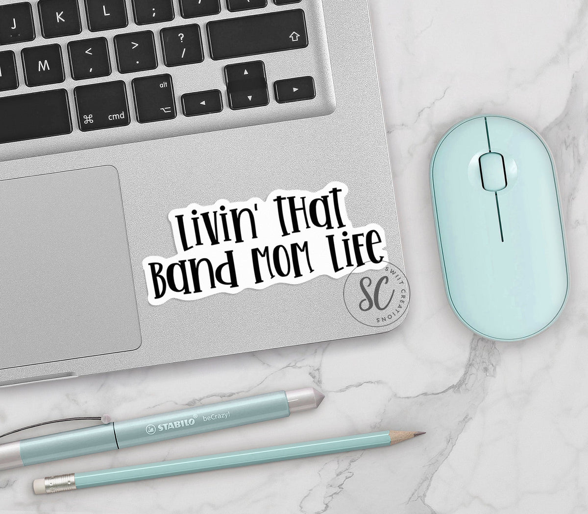 Black Band Mom Life vinyl sticker on a silver laptop next to a mint mouse and pens