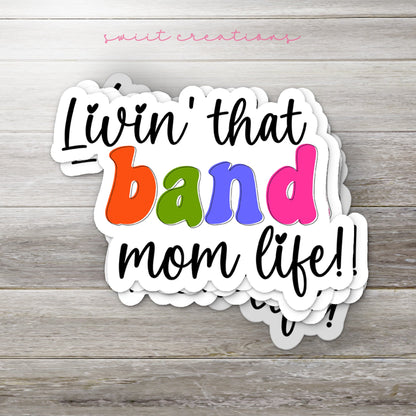 Stack of Rainbow Band Mom Life glossy stickers on a gray wood table