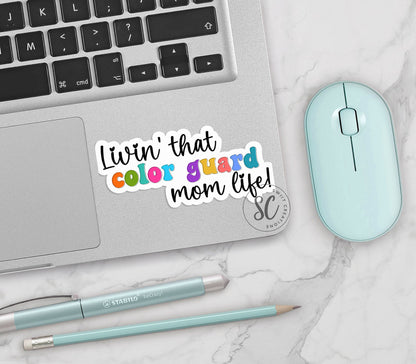 Rainbow Color Guard Mom Life vinyl sticker on a silver laptop next to a mint mouse and pens