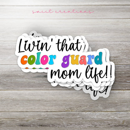 Stack of Rainbow Color Guard Mom Life glossy stickers on a gray wood table