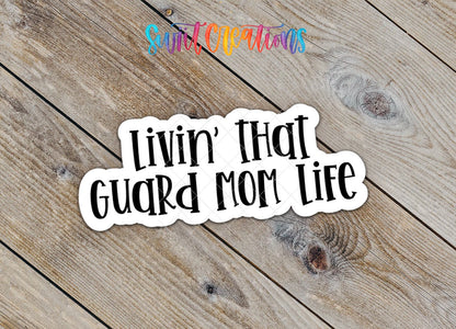 Close-up of the Livin' That Guard Mom Life sticker on rustic wood