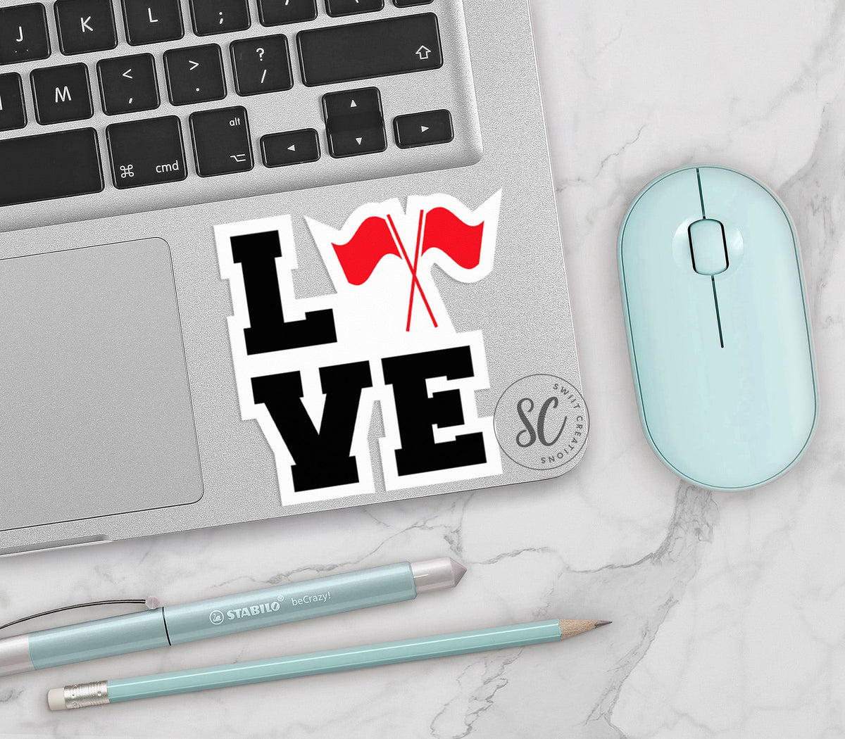 Red Love Color Guard vinyl sticker on a silver laptop next to a mint mouse and pens