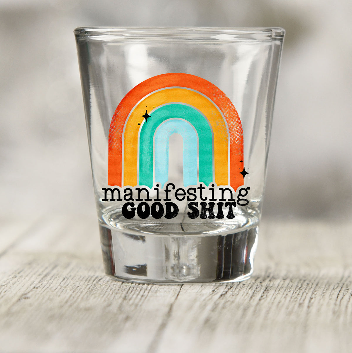 Manifesting Good Sh*t shot glass UV DTF transfer with retro rainbow with star accents on a clear shot glass
