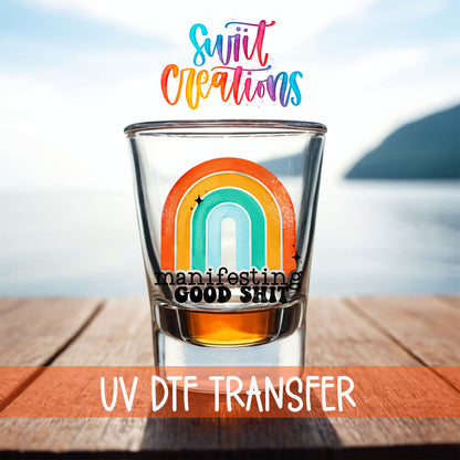 Manifesting Good Sh*t shot glass UV DTF transfer on a filled shot glass on a dock by the water