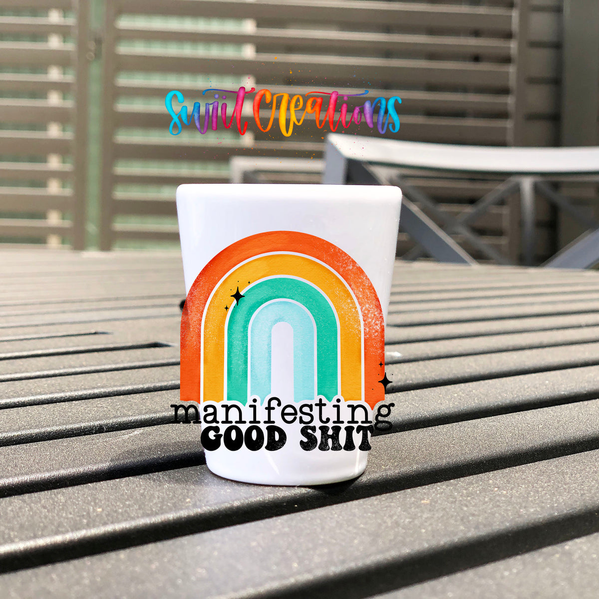 Manifesting Good Sh*t UV DTF transfer on a white shot glass on an outdoor patio table