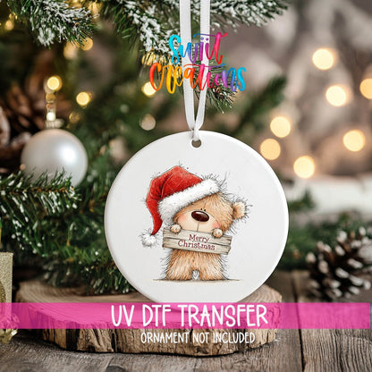 Merry Christmas Teddy Bear ornament UV DTF transfer on an ornament resting on a wood slice beside a Christmas tree