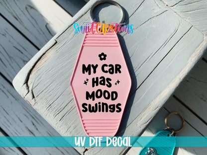 My Car Has Mood Swings UV DTF transfer on a pink motel keychain on a wood board