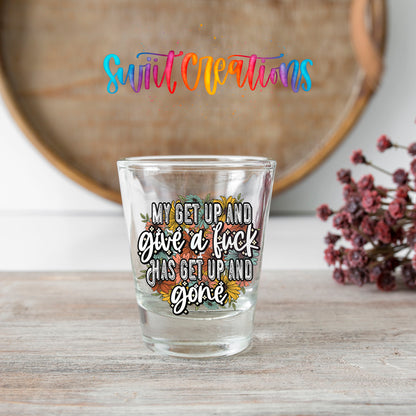 My Get Up and Give a F*ck shot glass transfer on a clear glass beside a wooden barrel and dried flowers
