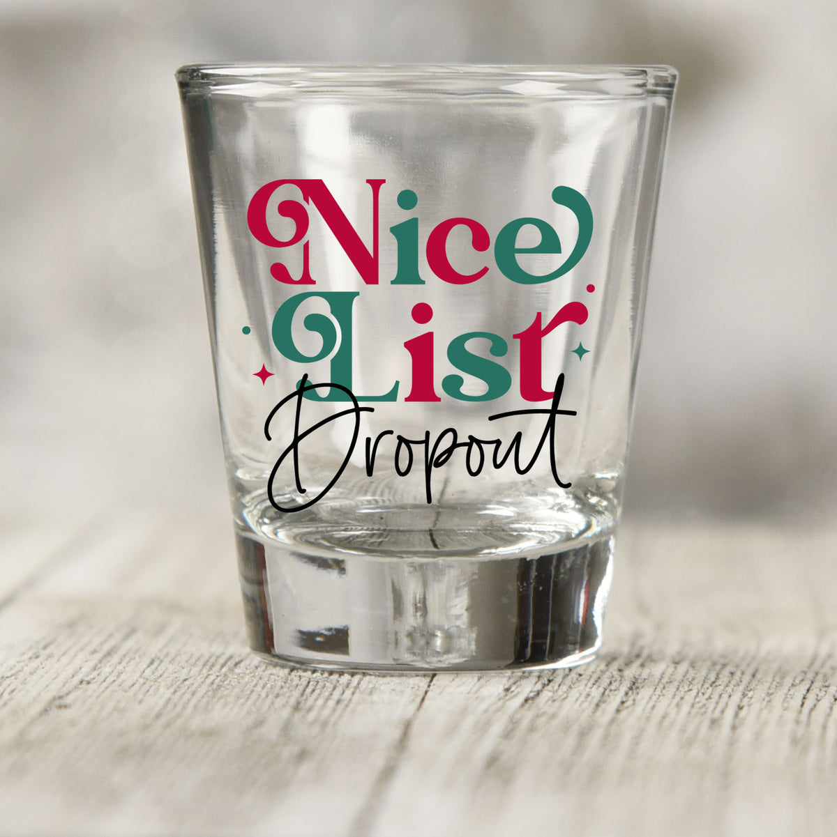 Nice List Dropout Christmas shot glass UV DTF transfer with red and green serif lettering with black script on a clear shot glass