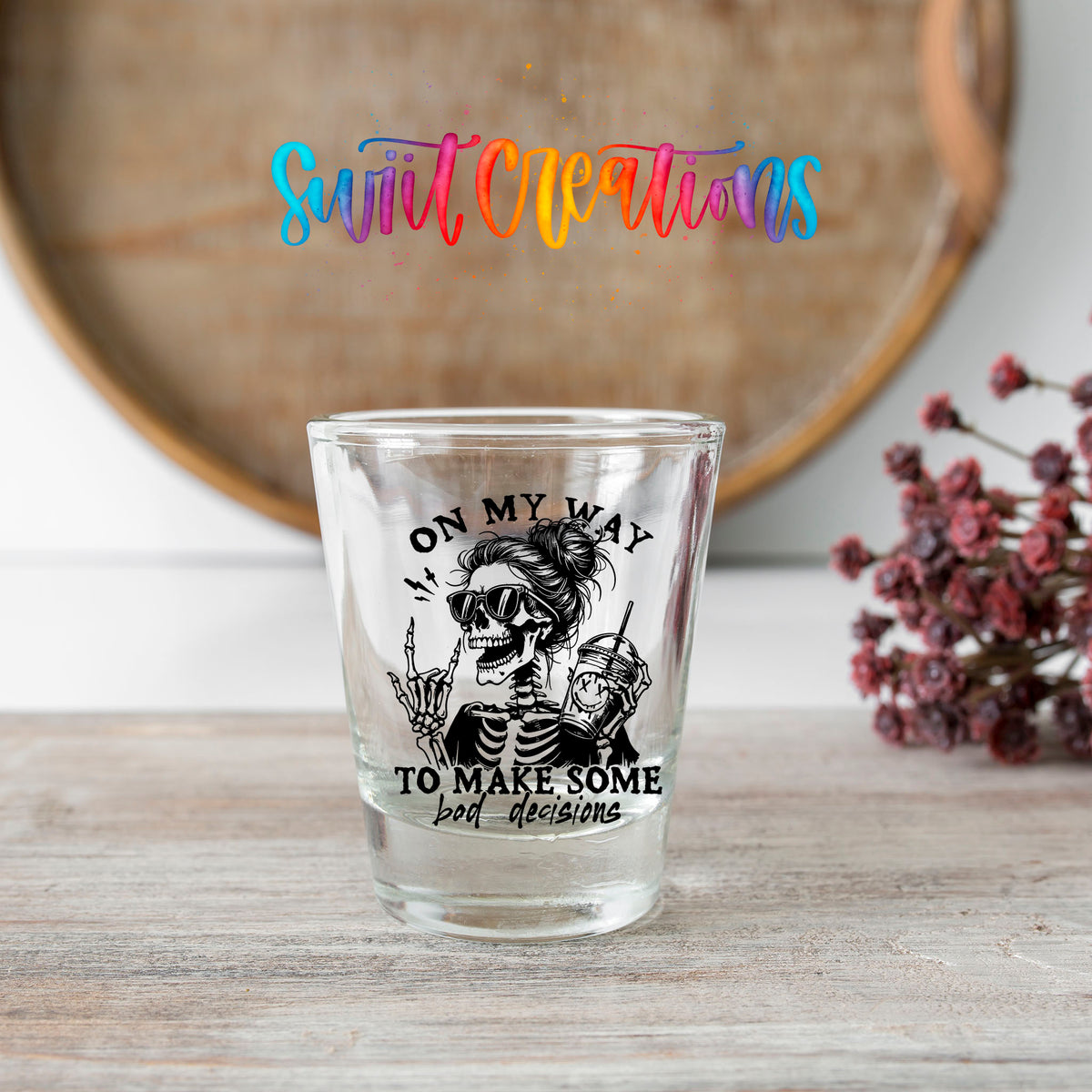 On My Way to Make Bad Decisions shot glass transfer on a clear glass beside a wooden barrel and dried flowers