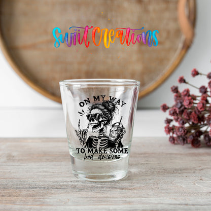 On My Way to Make Bad Decisions shot glass transfer on a clear glass beside a wooden barrel and dried flowers
