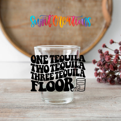 One Tequila Two Tequila shot glass transfer on a clear glass beside a wooden barrel and dried flowers