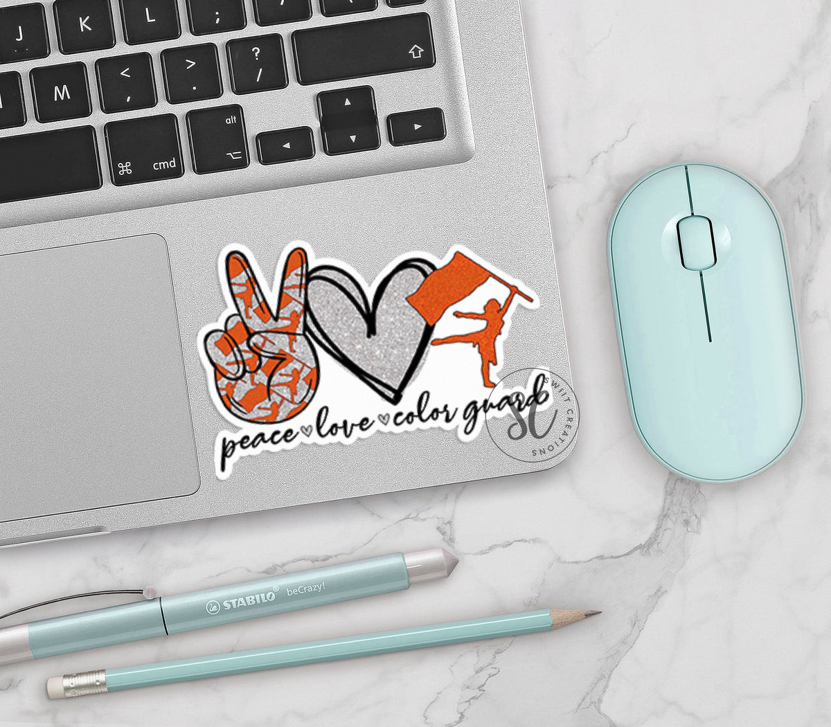 Orange Peace Love Color Guard vinyl sticker on a silver laptop next to a mint mouse and pens
