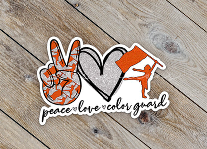 Close-up of the Orange Peace Love Color Guard sticker on rustic wood