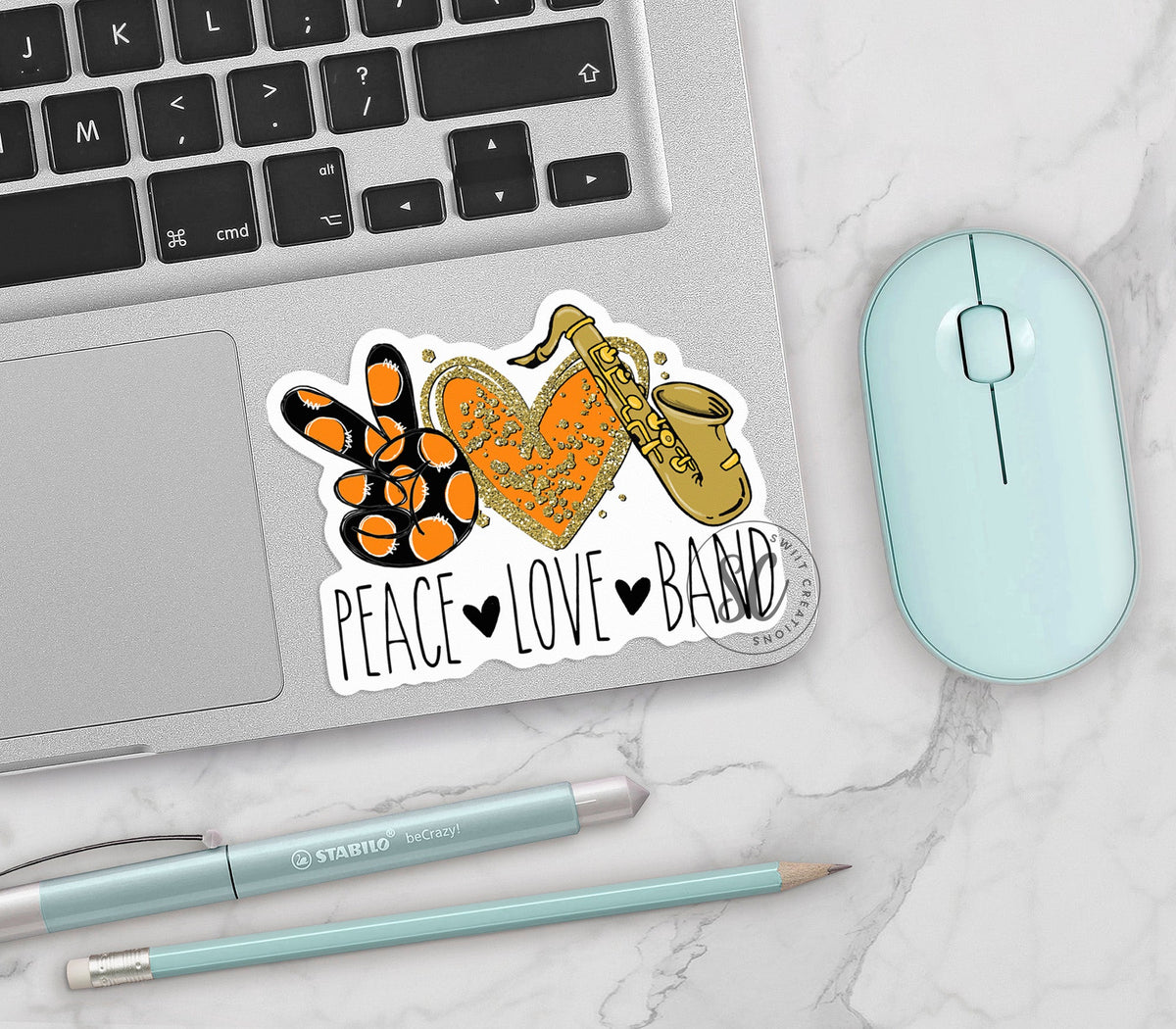 Peace Love Band Saxophone vinyl sticker on a silver laptop next to a mint mouse and pens