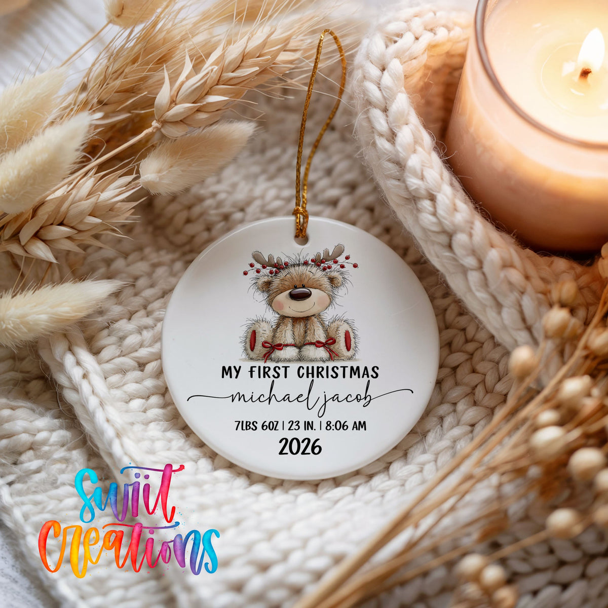 Personalized Baby’s First Christmas Reindeer Birth Stats ceramic ornament beside a lit candle and knit blanket