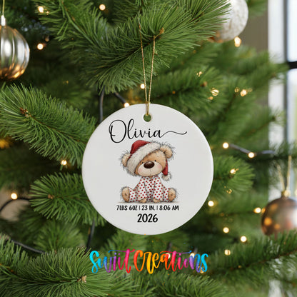 Personalized Baby’s First Christmas Santa Hat Teddy Bear ceramic ornament hanging on a lit green Christmas tree
