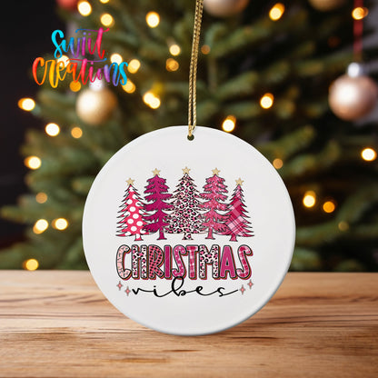 Pink Christmas Vibes Trees ornament UV DTF transfer on an ornament on a wooden table with tree lights behind it