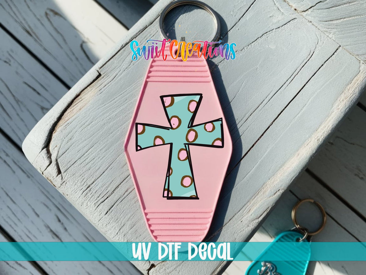 Polka Dot Cross UV DTF transfer on a pink motel keychain on a wood board