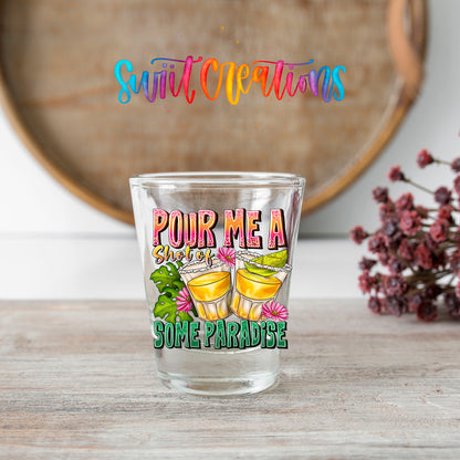 Pour Me a Shot of Some Paradise shot glass transfer on a clear glass beside a wooden barrel and dried flowers