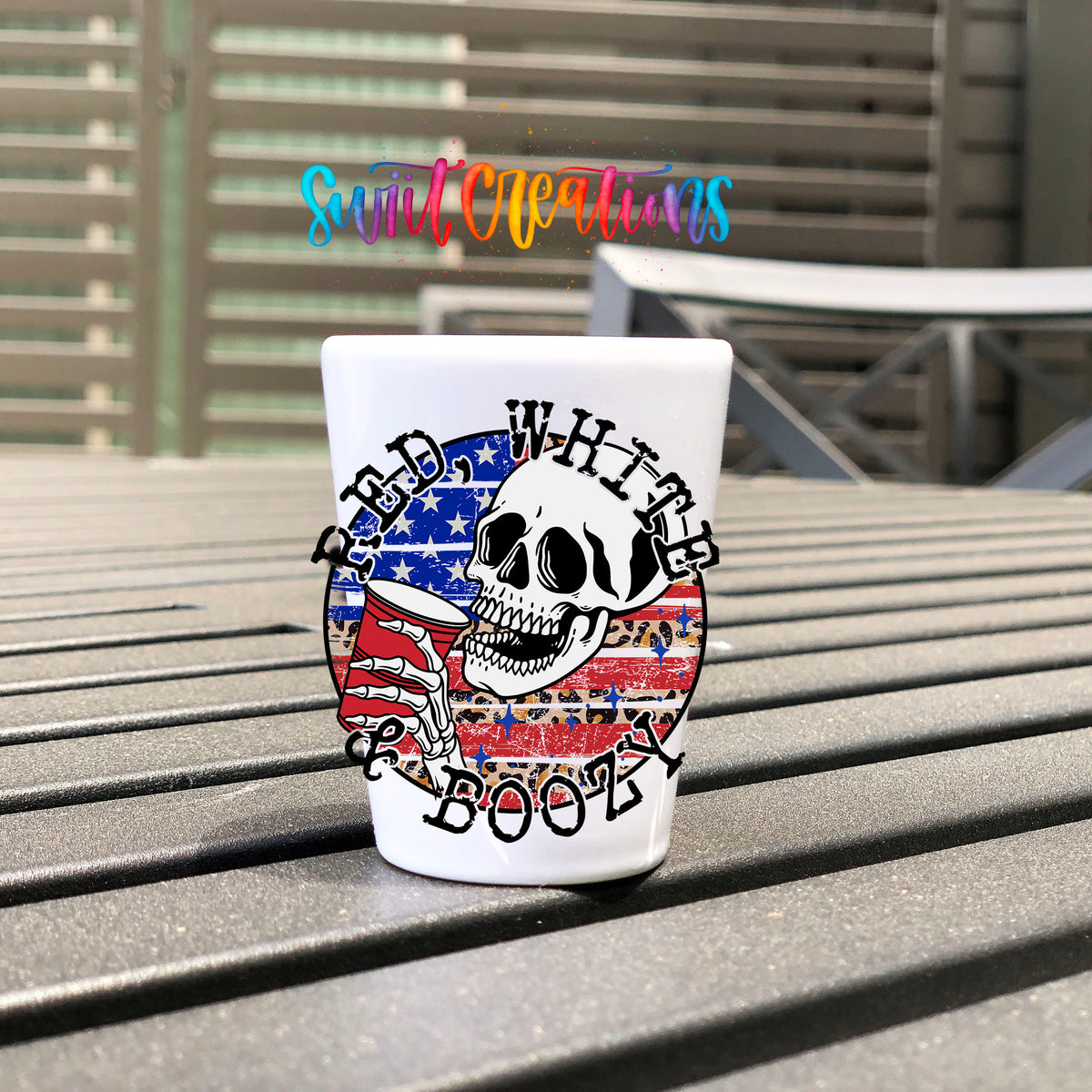 Red White and Boozy UV DTF transfer on a white shot glass on an outdoor patio table