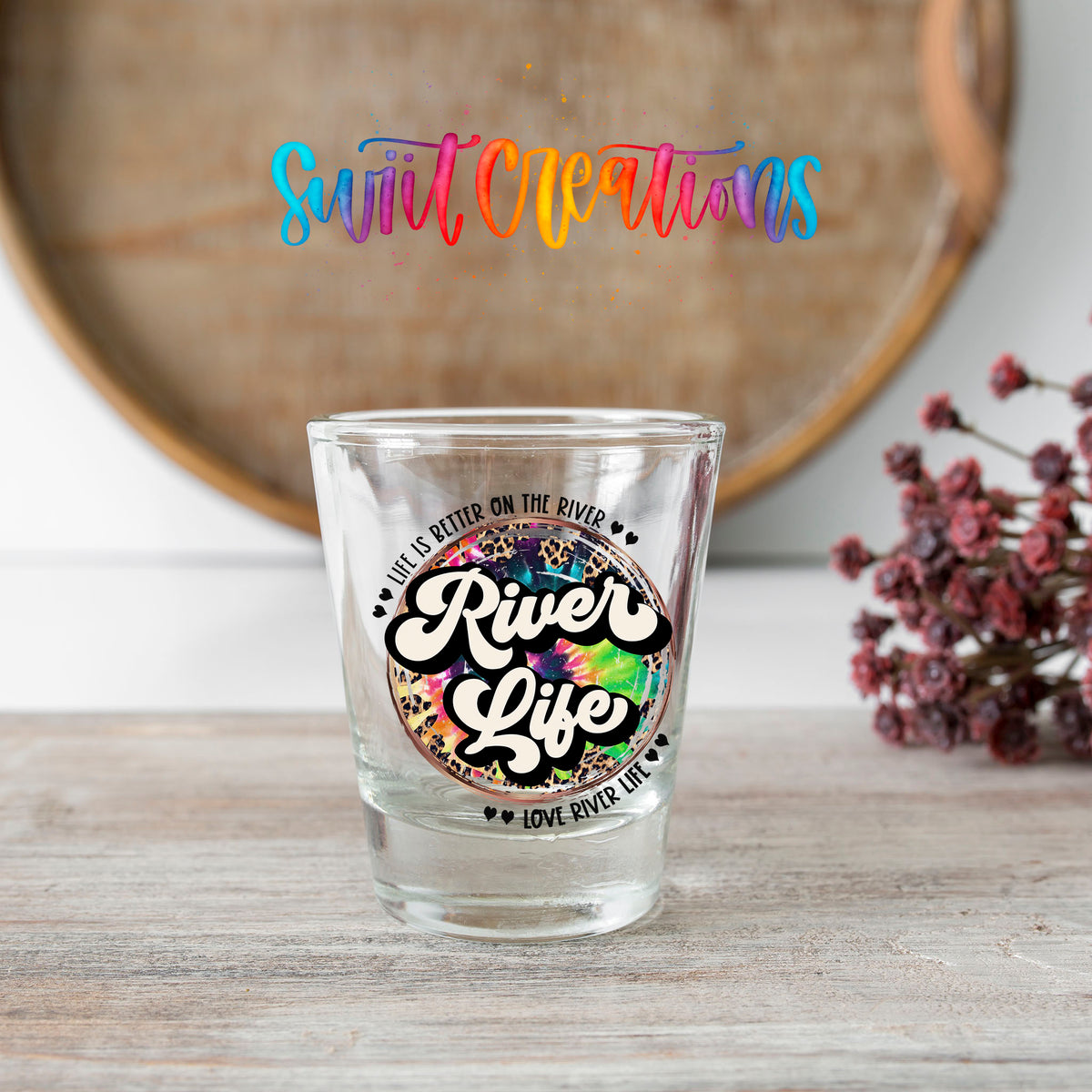 River Life shot glass transfer on a clear glass beside a wooden barrel and dried flowers