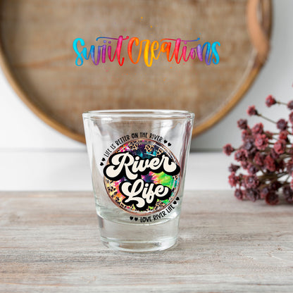 River Life shot glass transfer on a clear glass beside a wooden barrel and dried flowers