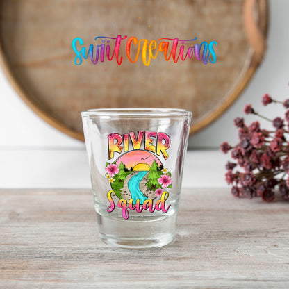 River Squad shot glass transfer on a clear glass beside a wooden barrel and dried flowers