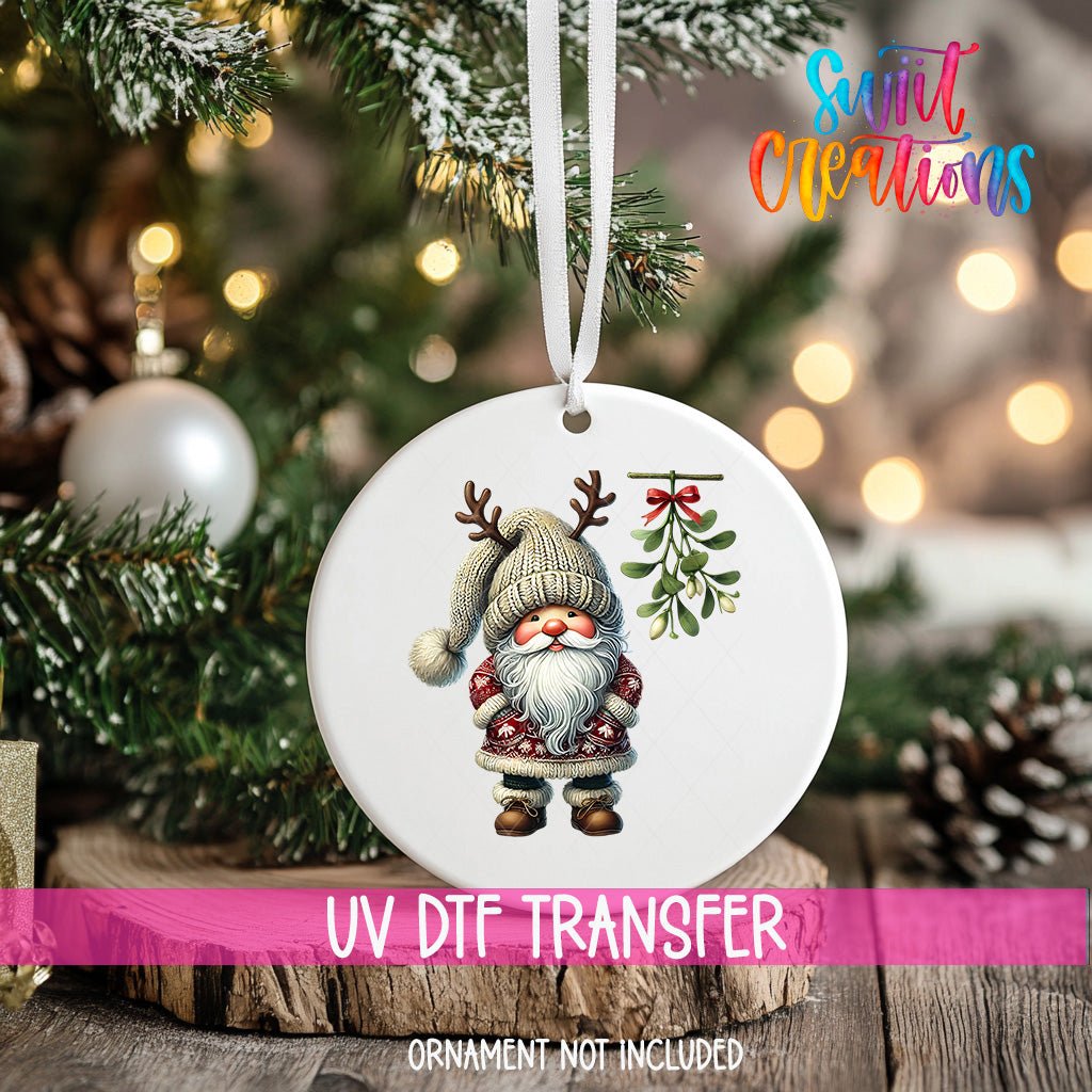 Santa Gnome Under Mistletoe ornament UV DTF transfer on an ornament resting on a wood slice beside a Christmas tree