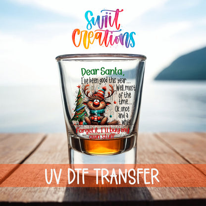 Santa I've Been Good Christmas shot glass UV DTF transfer on a filled shot glass on a dock by the water
