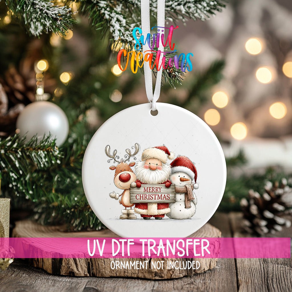 Santa Reindeer and Snowman ornament UV DTF transfer on an ornament resting on a wood slice beside a Christmas tree