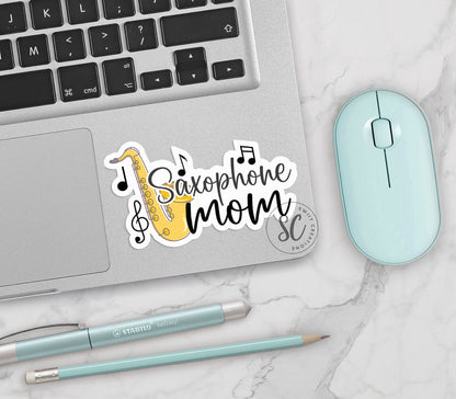 Saxophone Mom vinyl sticker on a silver laptop next to a mint mouse and pens