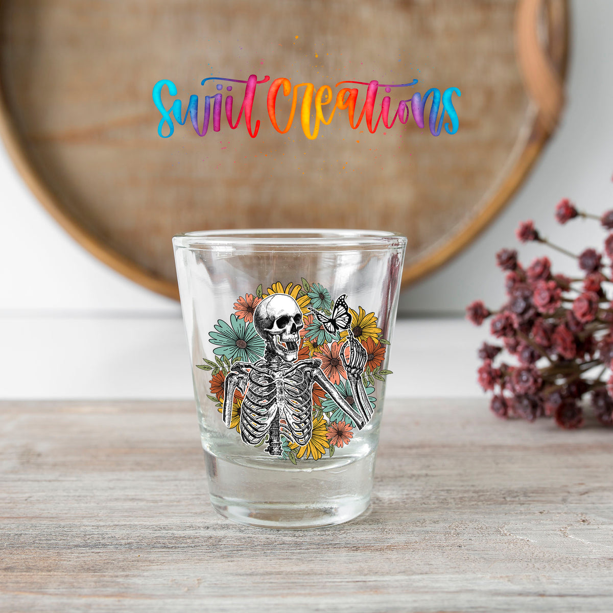 Skeleton Floral shot glass transfer on a clear glass beside a wooden barrel and dried flowers