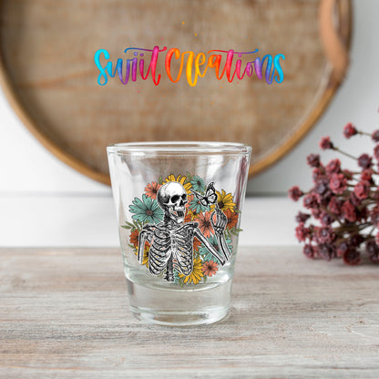 Skeleton Floral shot glass transfer on a clear glass beside a wooden barrel and dried flowers