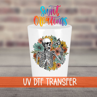 Skeleton Floral UV DTF transfer on a white shot glass in front of a brick wall