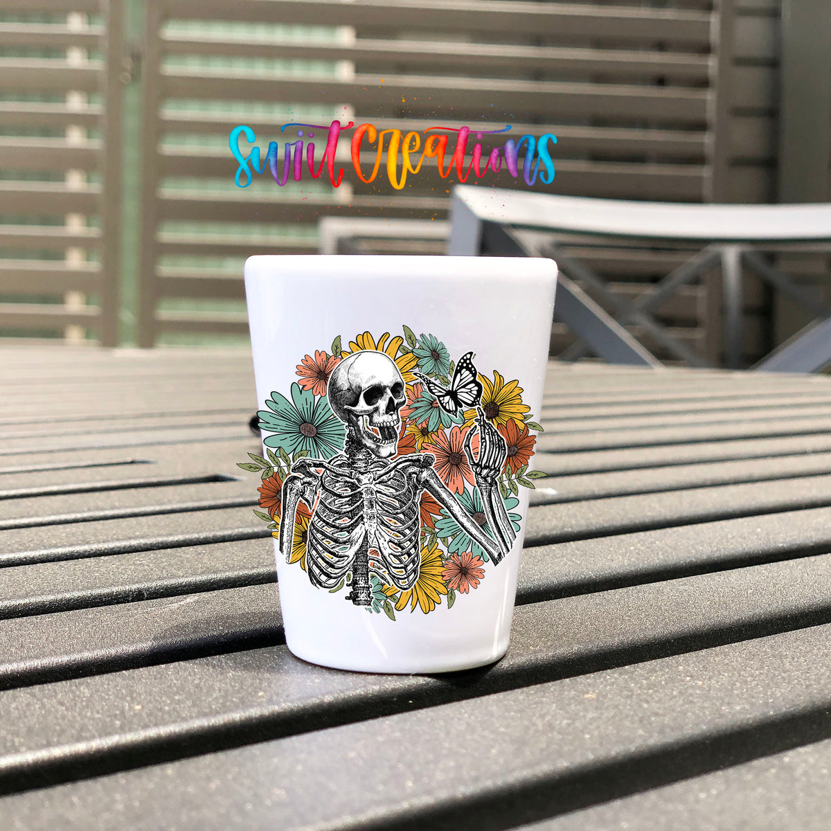 Skeleton Floral UV DTF transfer on a white shot glass on an outdoor patio table