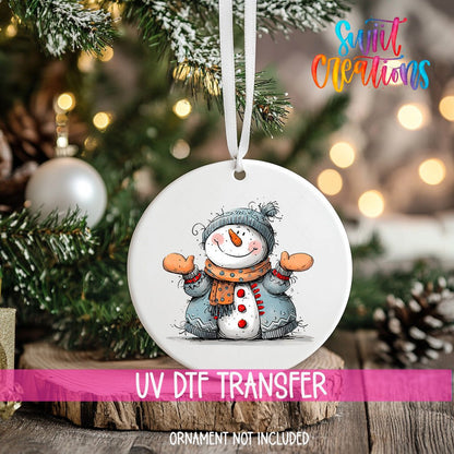 Snowman with Open Arms ornament UV DTF transfer on an ornament resting on a wood slice beside a Christmas tree