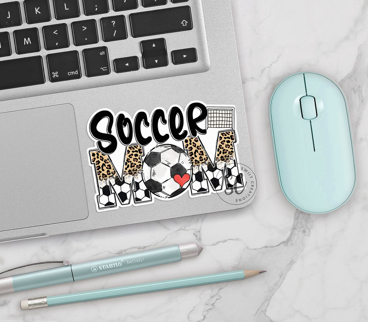 Soccer Mom vinyl sticker on a silver laptop next to a mint mouse and pens