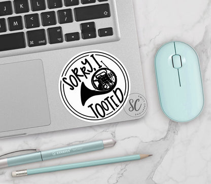 Sorry I Tooted French Horn vinyl sticker on a silver laptop next to a mint mouse and pens