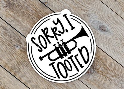 Close-up of the Sorry I Tooted Trumpet sticker on rustic wood