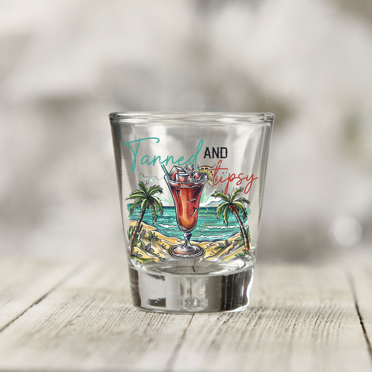 Close-up of the Tanned and Tipsy UV DTF transfer on a clear shot glass