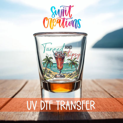 Tanned and Tipsy shot glass UV DTF transfer on a filled shot glass on a dock by the water