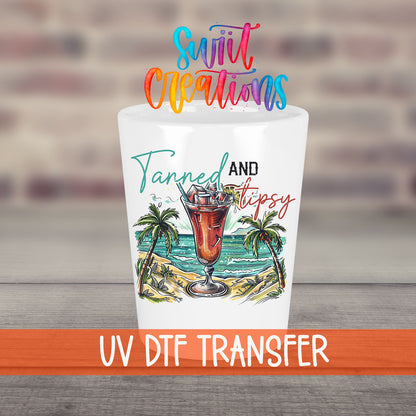 Tanned and Tipsy UV DTF transfer on a white shot glass in front of a brick wall