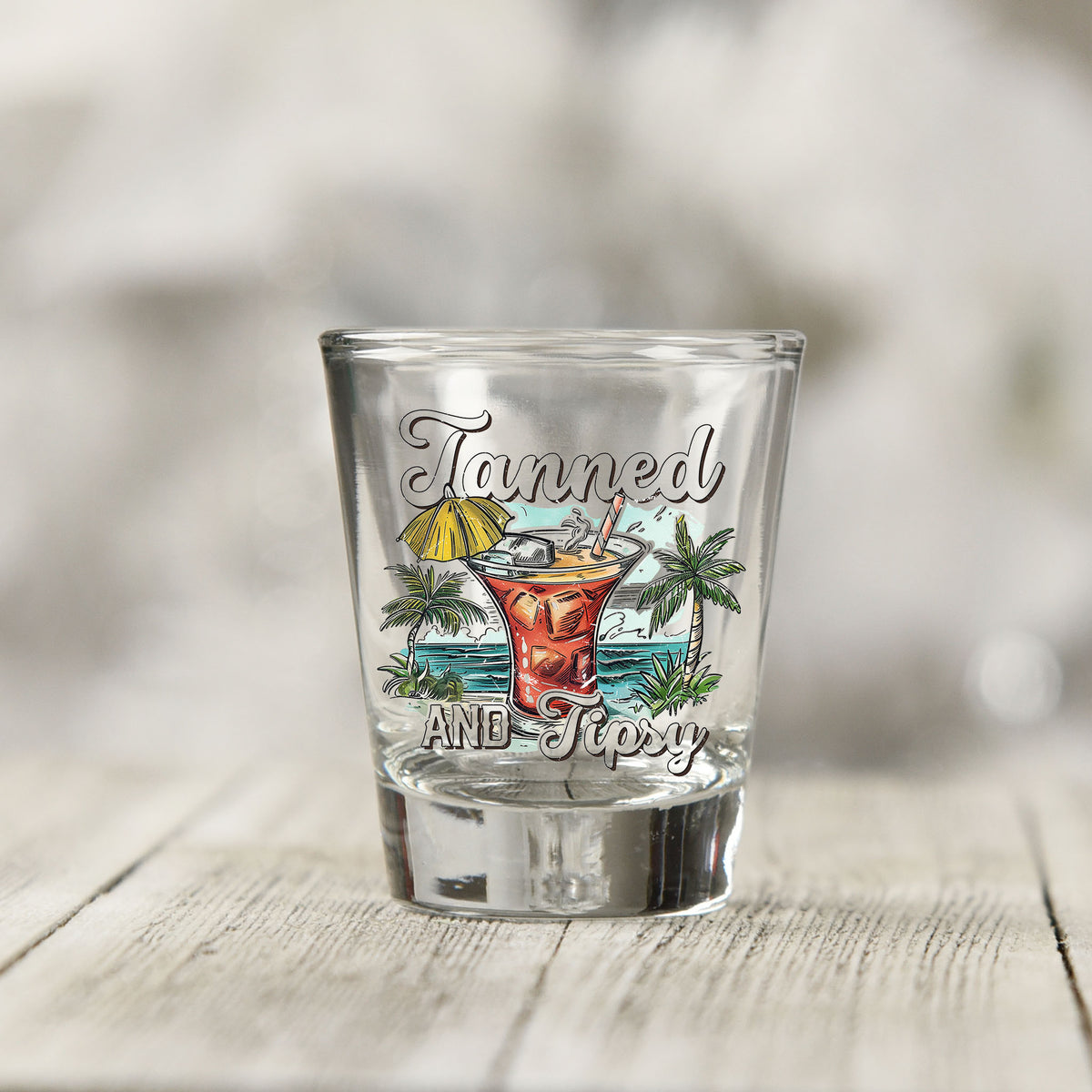 Close-up of the Tanned and Tipsy UV DTF transfer on a clear shot glass